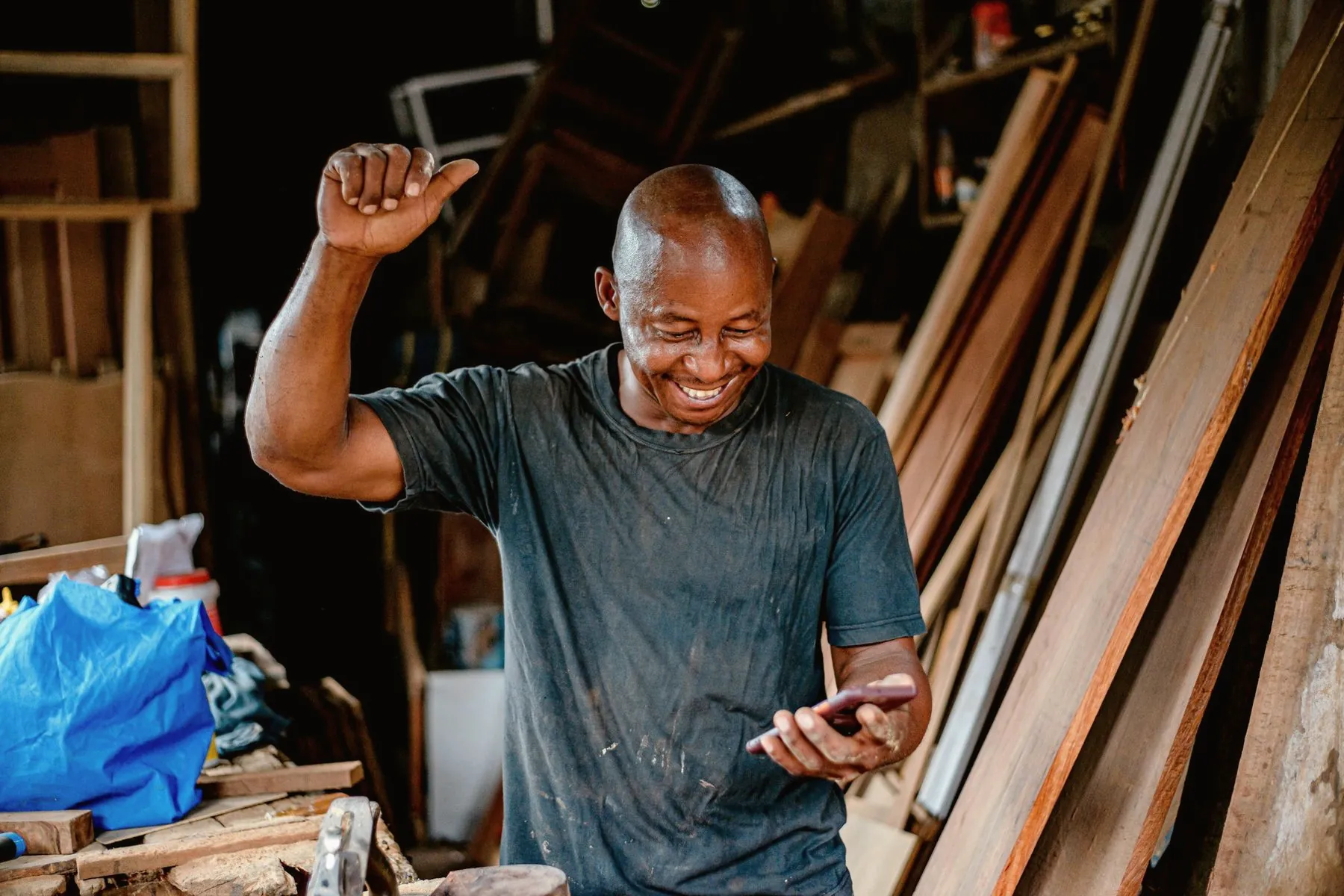 A carpenter in his workshop grinning at his phone, one fist raised
